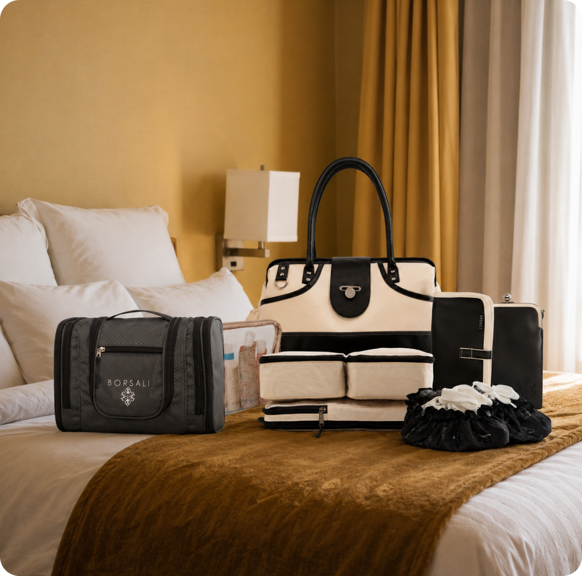A collection of travel and luggage items arranged on a bed in a warmly lit hotel room. The set includes a black ROPSALI duffel bag, a cream and black structured handbag, a matching cream and black zip case, a black and cream flat case, a clear toiletry bag with a blue cap, and a black ruffled accessory.